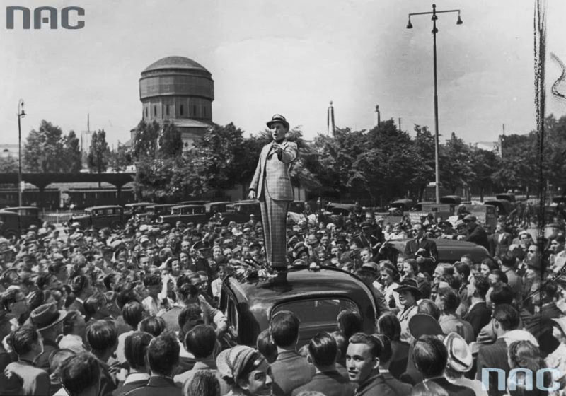 Jan Kiepura śpiewa przed dworcem kolejowym z dachu samochodu dla witającej go publiczności, 1938, Poznań, fot. Narodowe Archiwum Cyfrowe (NAC)